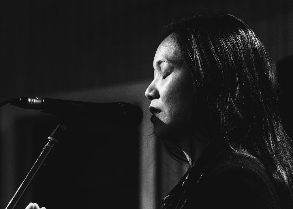 Black and white photo of a poet speaking into a microphone.